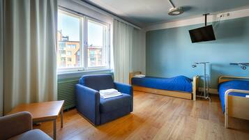 Hotellihuone, jossa on sänky, tuoli, työpöytä, televisio ja ikkuna, jossa on verhot.