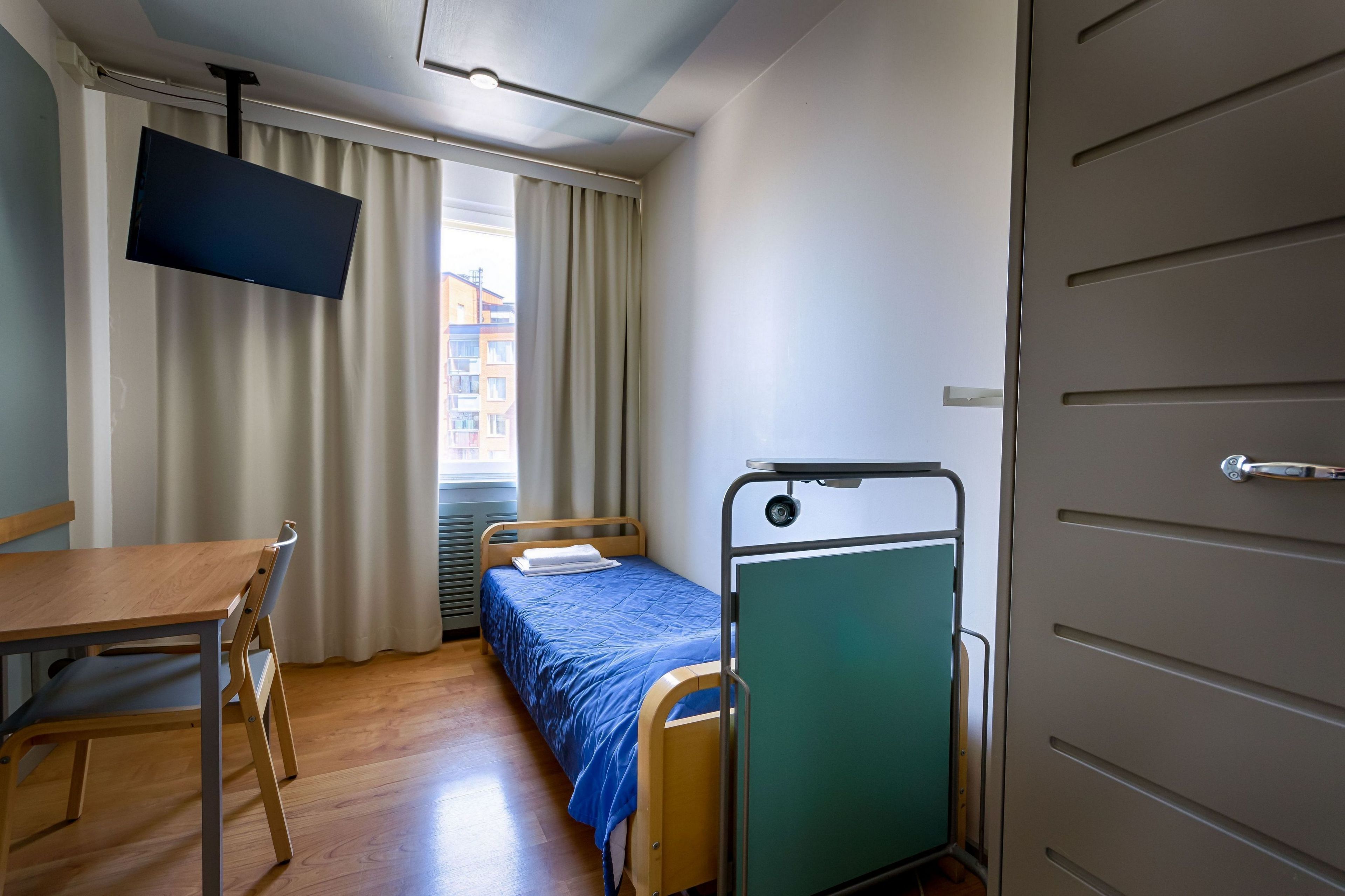 A small, compact room with a single bed, a desk, and a chair.