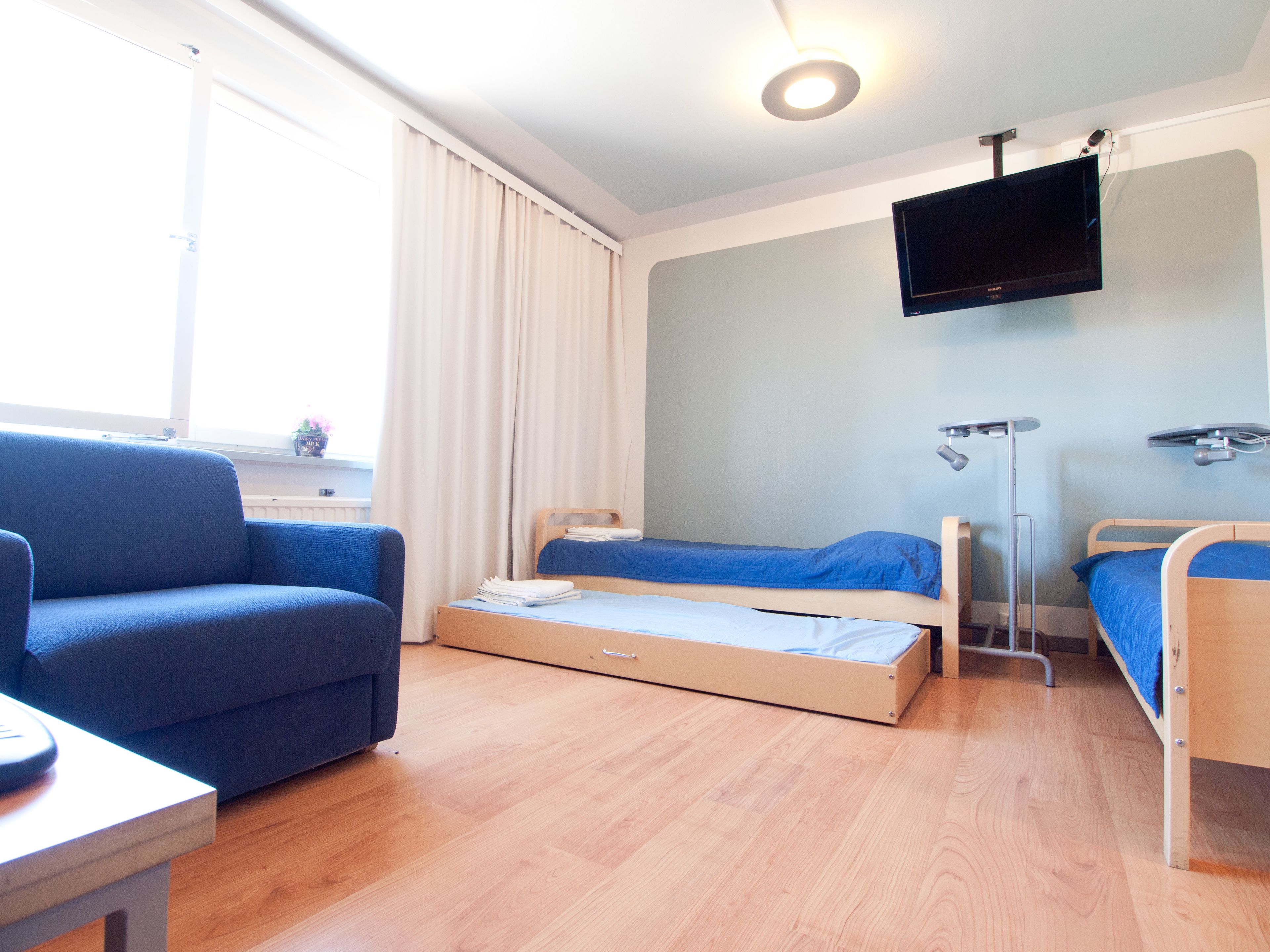 A room with a blue sofa, two single beds, a TV, and a desk.