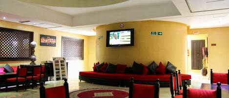 Un hall de hotel con un sofá rojo, sillas rojas, un televisor y un cartel que indica una salida.