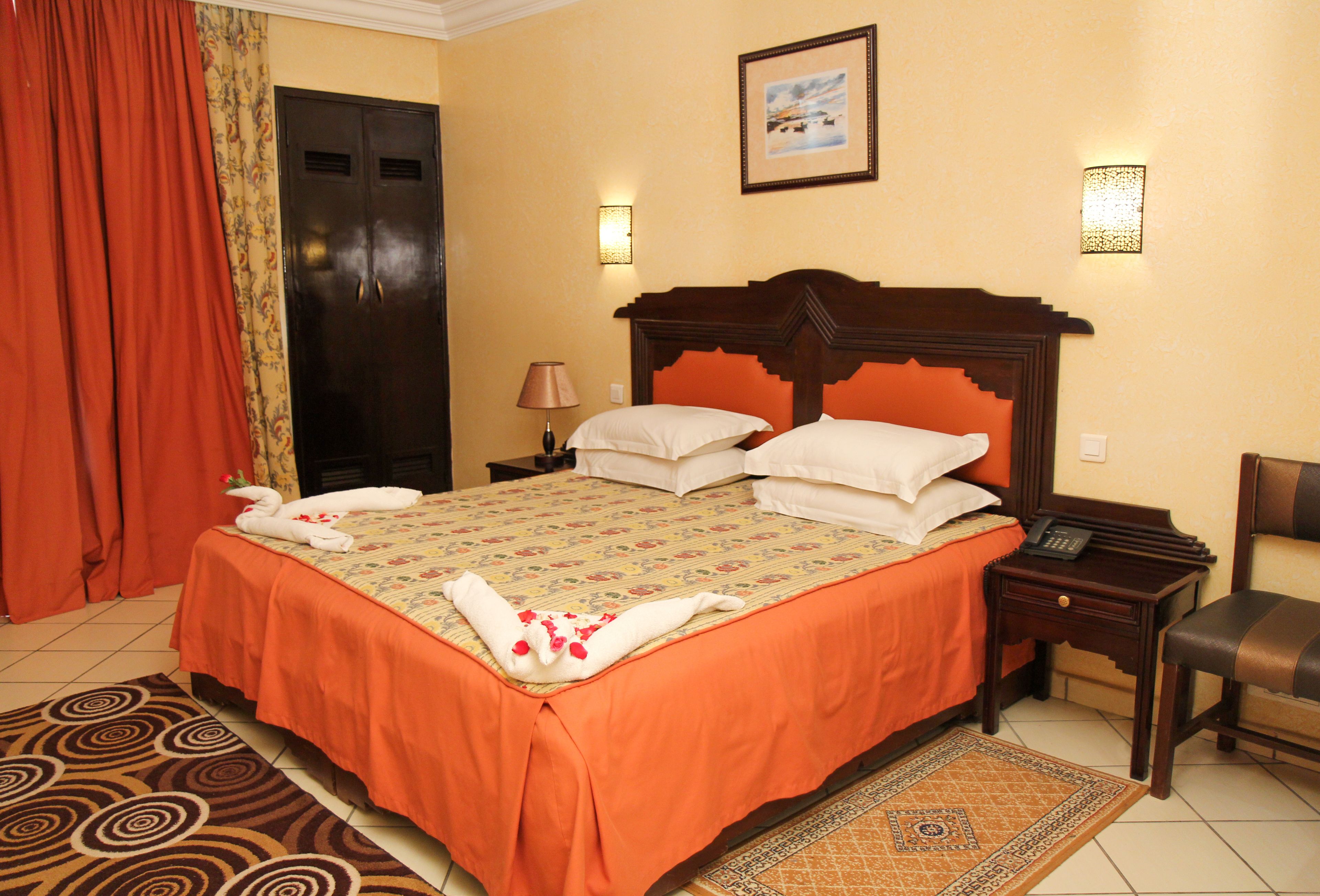 Een hotelkamer met een groot bed, een nachtkastje met een lamp, een stoel en een deur.