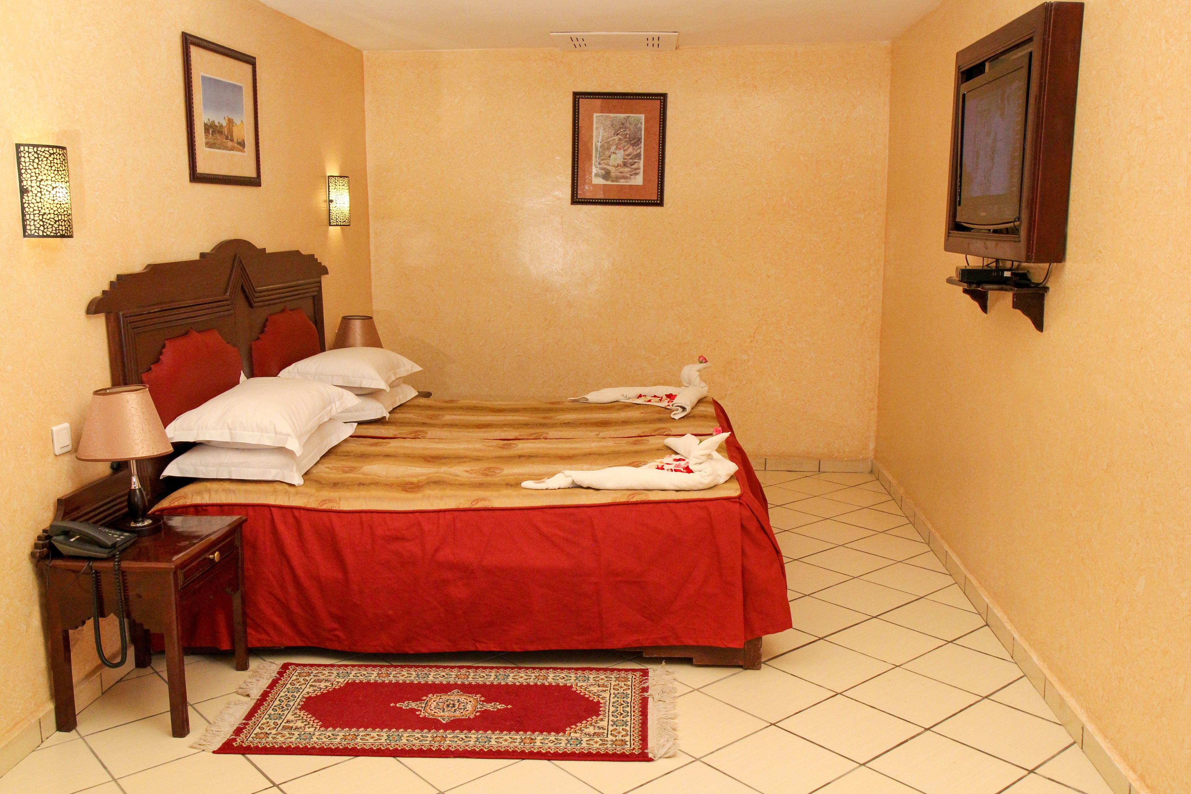 Una habitación de hotel con una cama, una mesita de noche con una lámpara, un teléfono y un televisor montado en la pared.