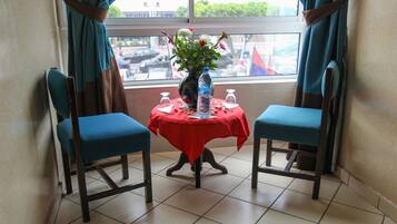 A room with two blue chairs, a small table with a red tablecloth, a vase with flowers, and a water bottle.