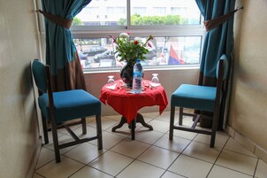 Una stanza con due sedie blu, un tavolino con una tovaglia rossa, un vaso con fiori e una bottiglia d'acqua.