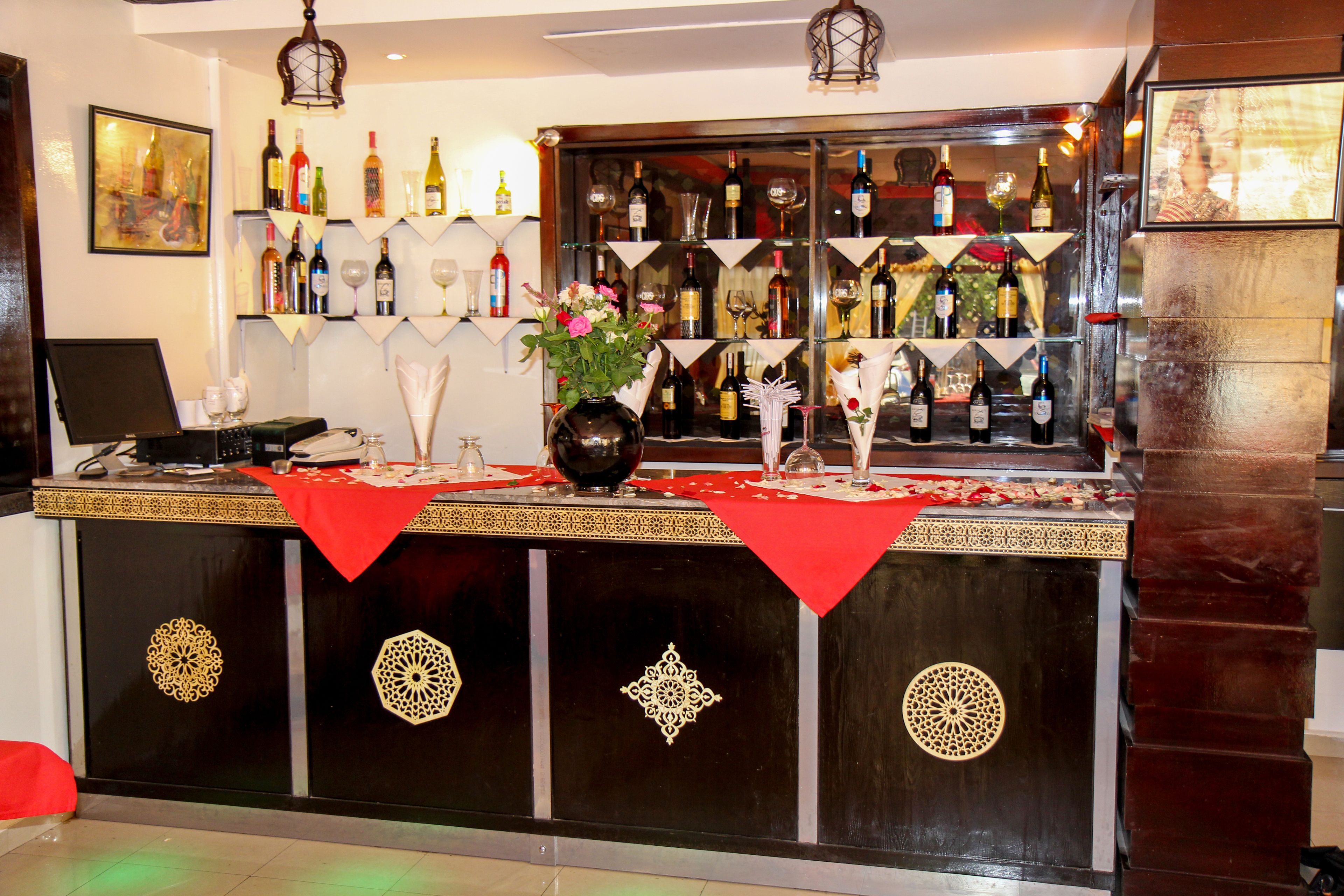 A bar area with shelves of bottles and glasses, a laptop, and decorative items.