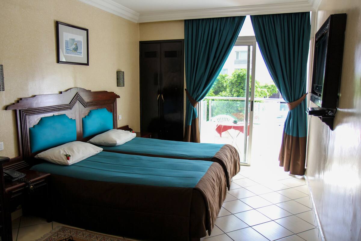 Habitación de hotel con dos camas, un armario, un televisor y un balcón con cortinas.