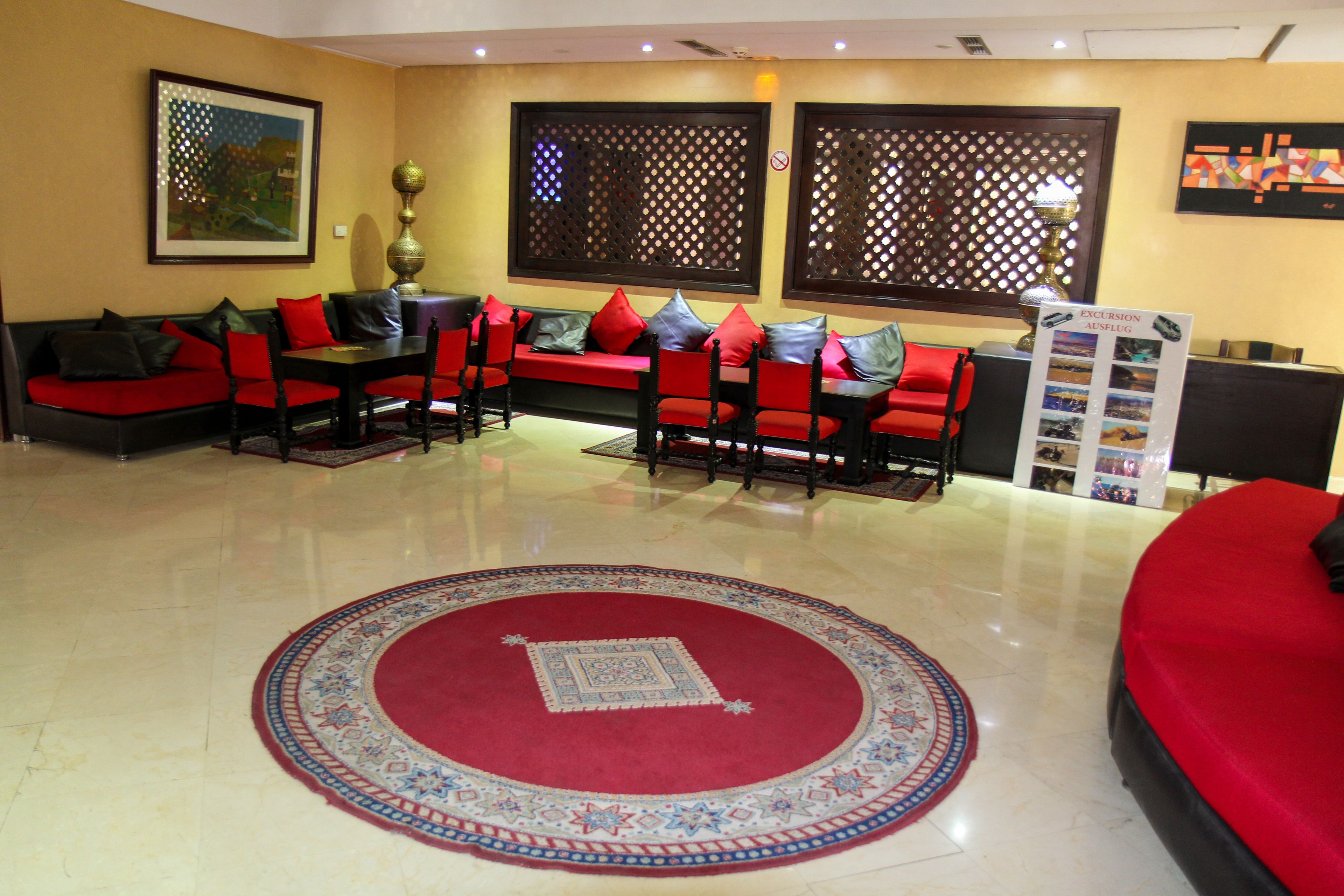 A lobby with a red sofa, red chairs, a round red carpet, and a reception desk with a sign.