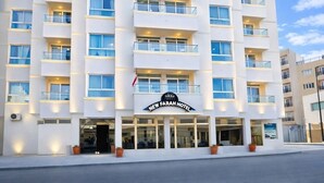Un hotel de varios pisos con fachada plana, grandes ventanales y un cartel que dice 'New Farah Hotel'.