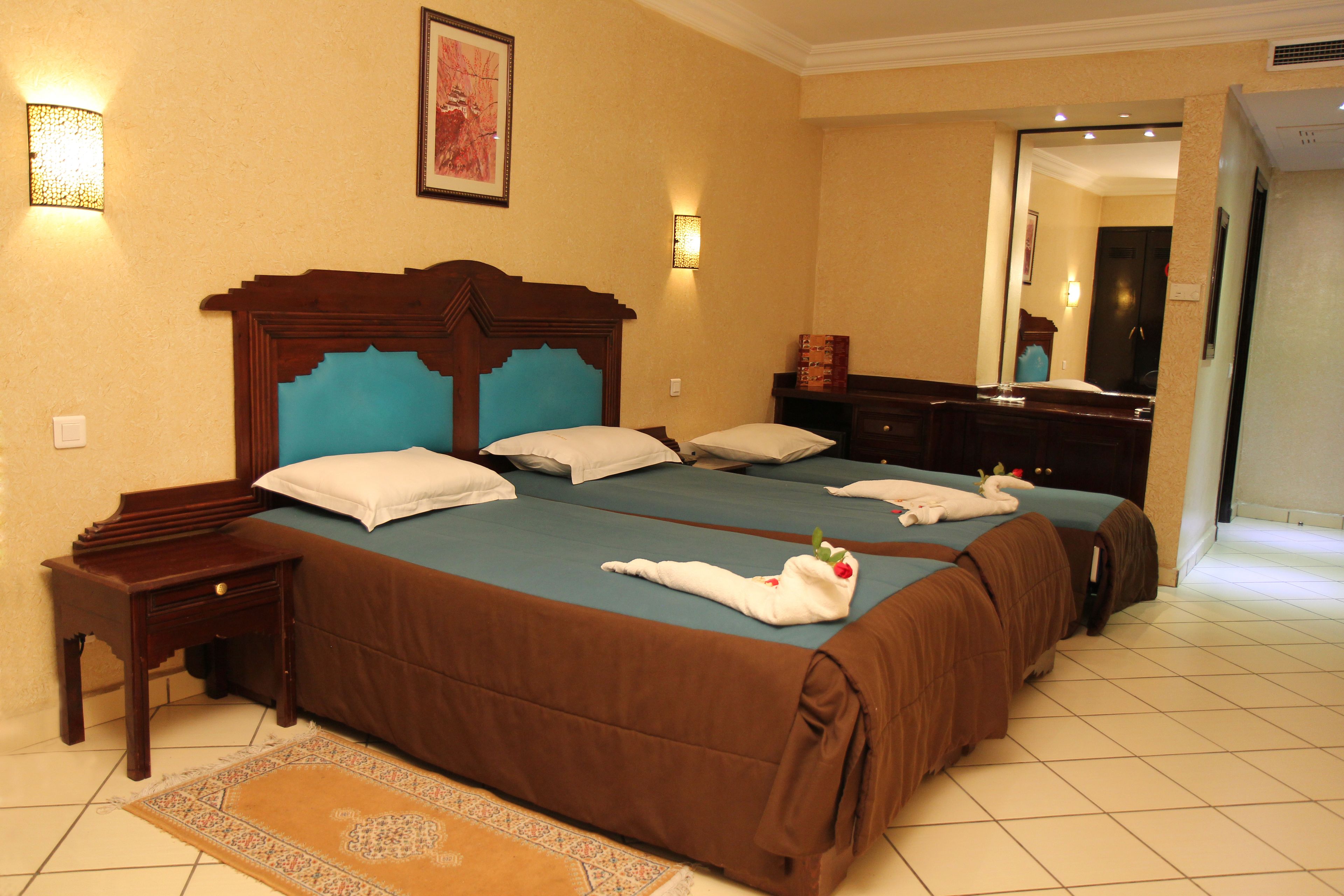 A hotel room with a large bed, two bedside tables, a nightstand, a mirror, and a wall-mounted light fixture.