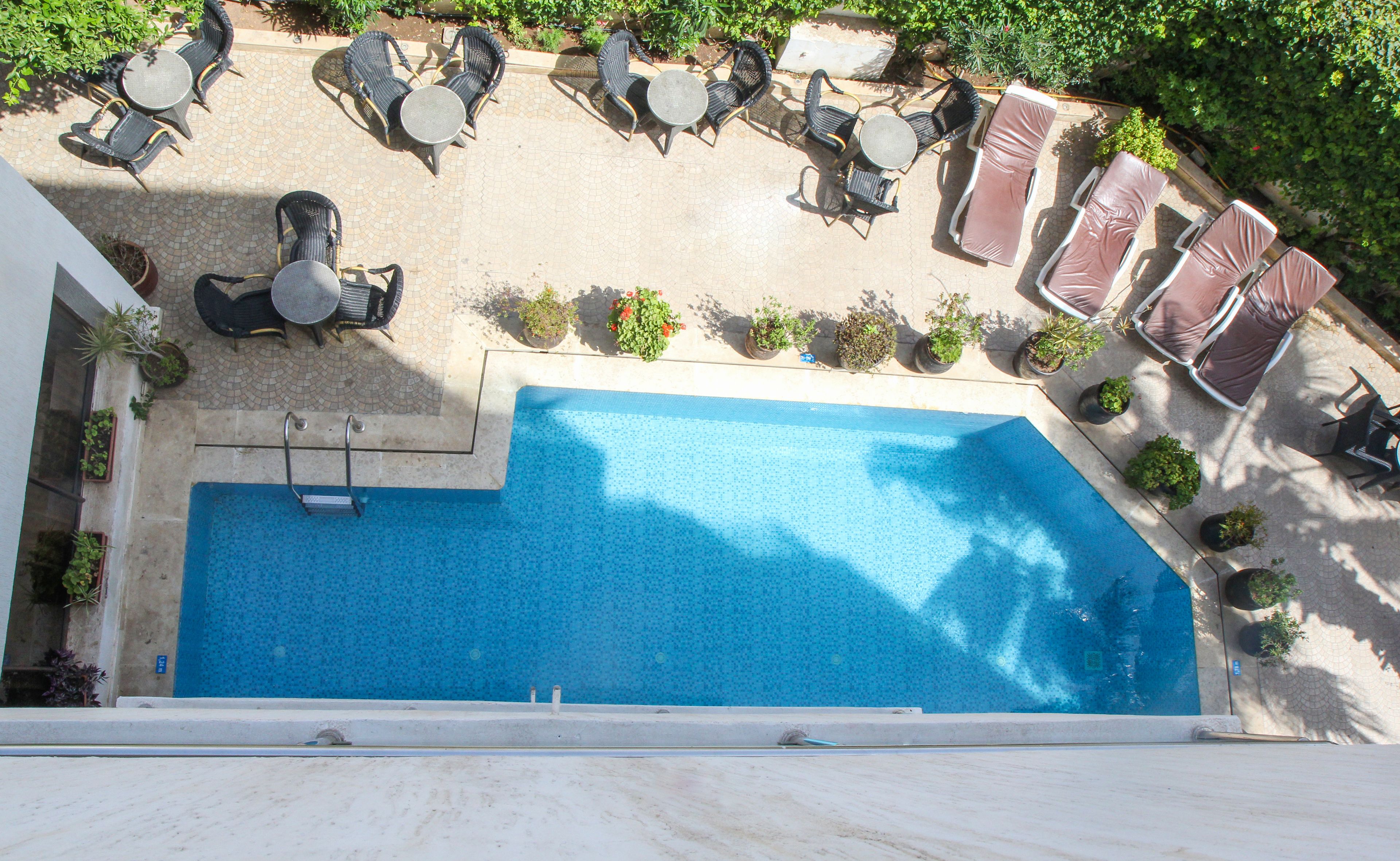 An outdoor swimming pool with lounge chairs and tables, surrounded by potted plants.