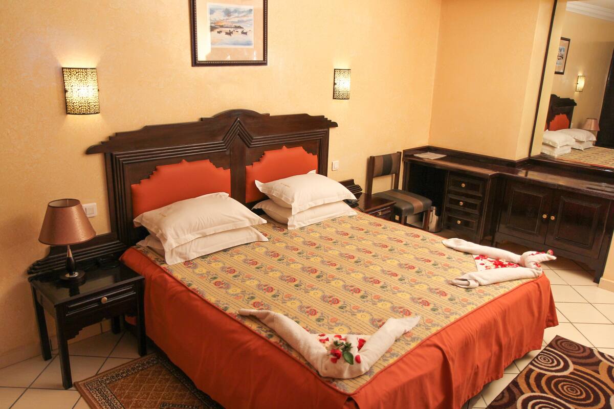 Una habitación de hotel con una cama grande, una mesita de noche con lámpara, un aparador y un espejo.