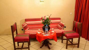 A room with a sofa, two chairs, a small table with a vase of flowers, and a bottle of water.