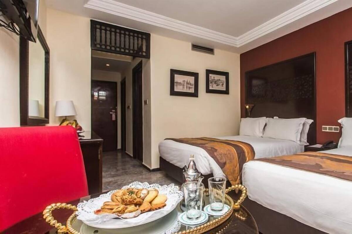 A hotel room with two beds, a dining table with food and drinks, and a red chair.