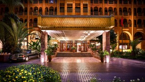 A hotel entrance with a covered walkway, palm trees, and a car parked in front. - El Andalous Lounge & Spa Hotel (Marrakech)