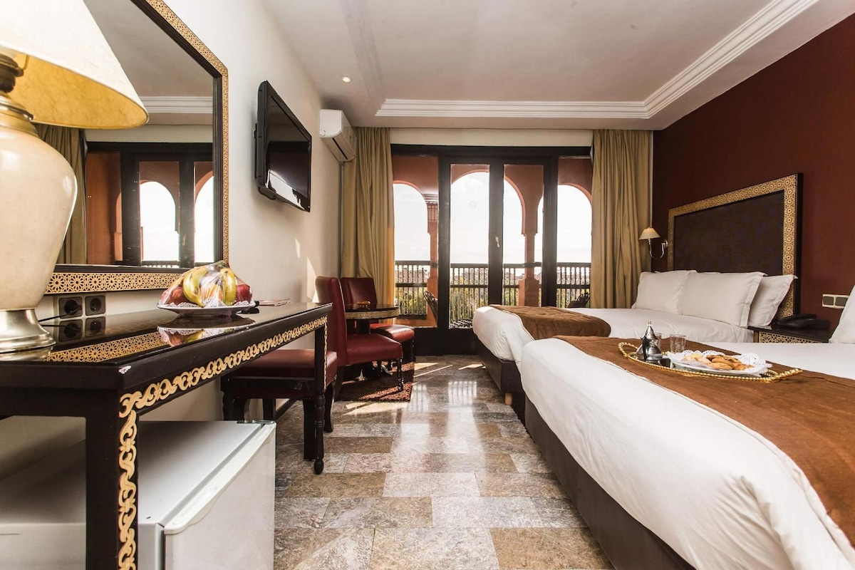 A hotel room with a bed, a desk, a chair, a TV, and a balcony with a view.