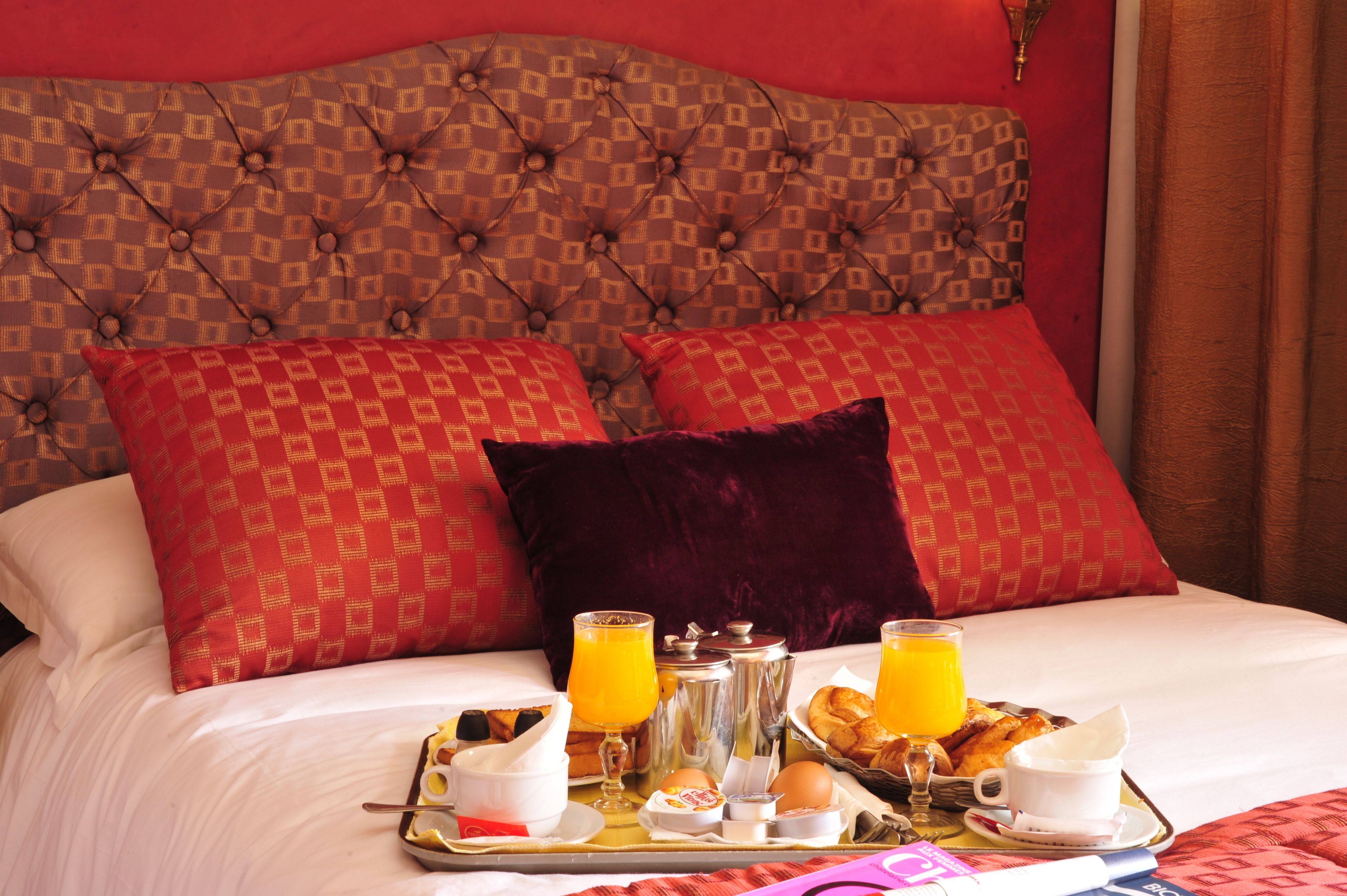 A neatly made bed with a patterned headboard, red pillows, and a tray with breakfast items including eggs, toast, and orange juice.