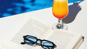 Una copa de cóctel con un borde rojo y una decoración sobre un libro abierto, con gafas a un lado.