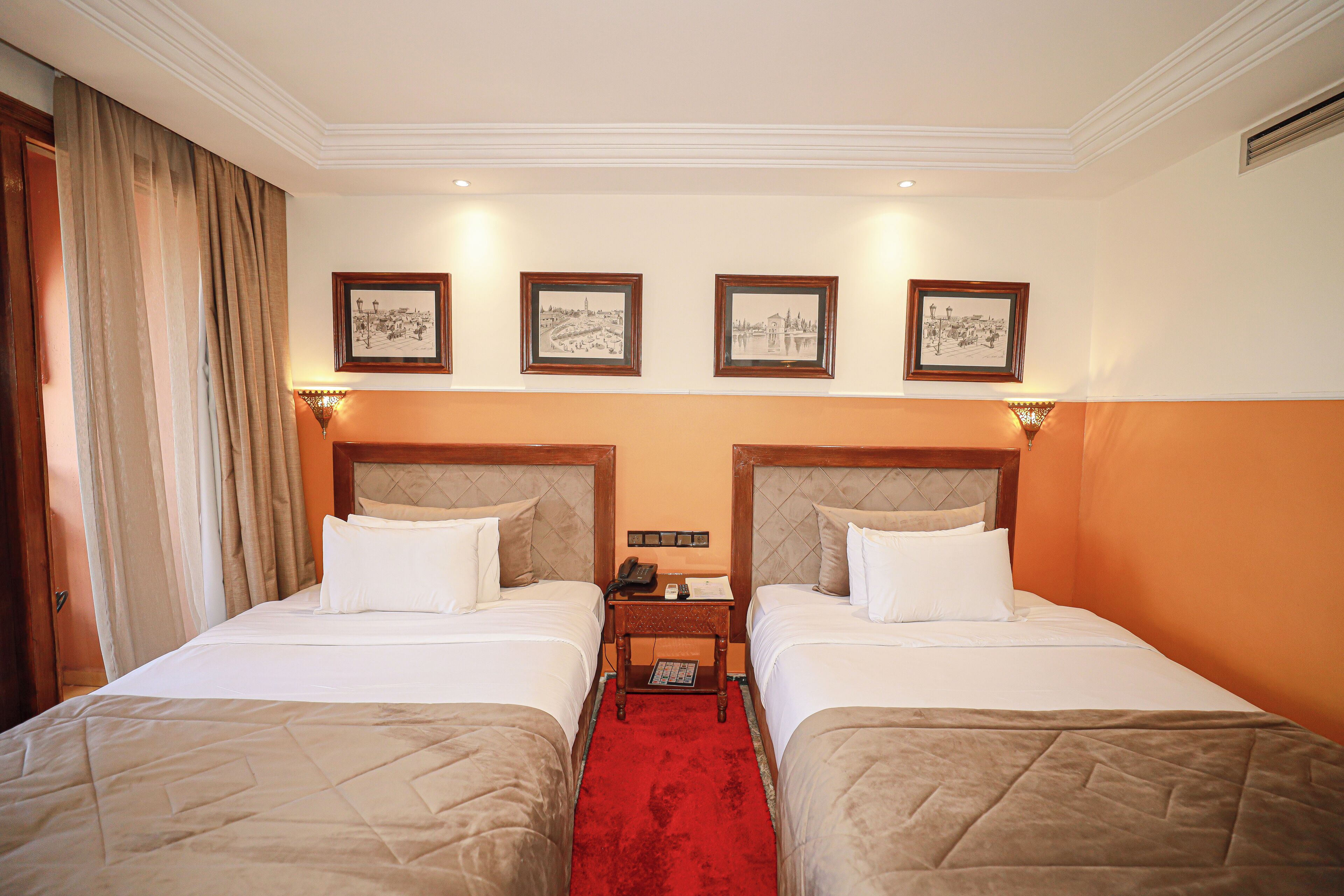 A hotel room with two beds, a red carpet, and framed pictures on the wall.
