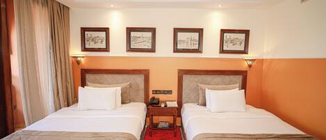 A hotel room with two beds, a red carpet, and framed pictures on the wall.