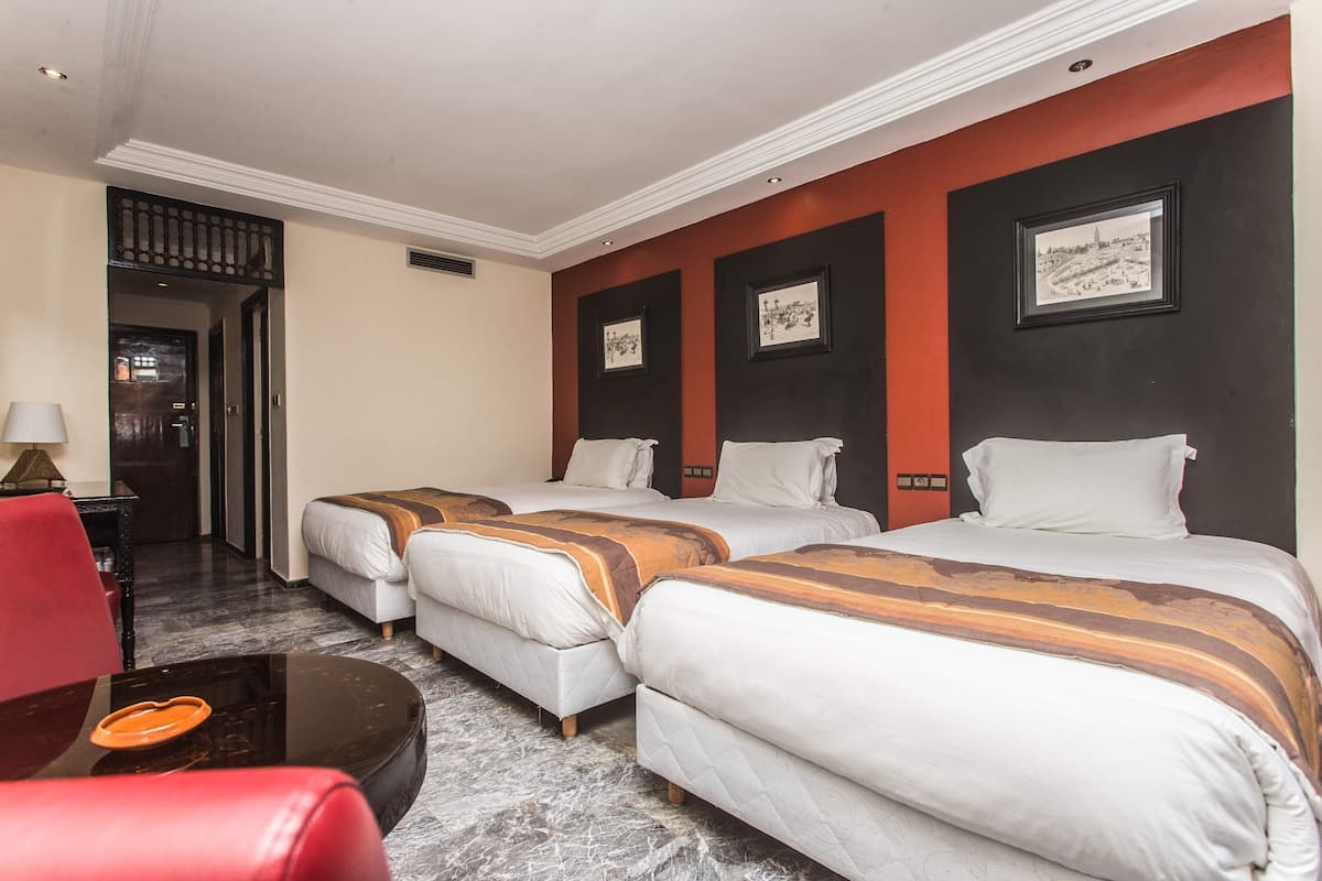 A hotel room with two beds, a red chair, a small table, and a framed picture on the wall.