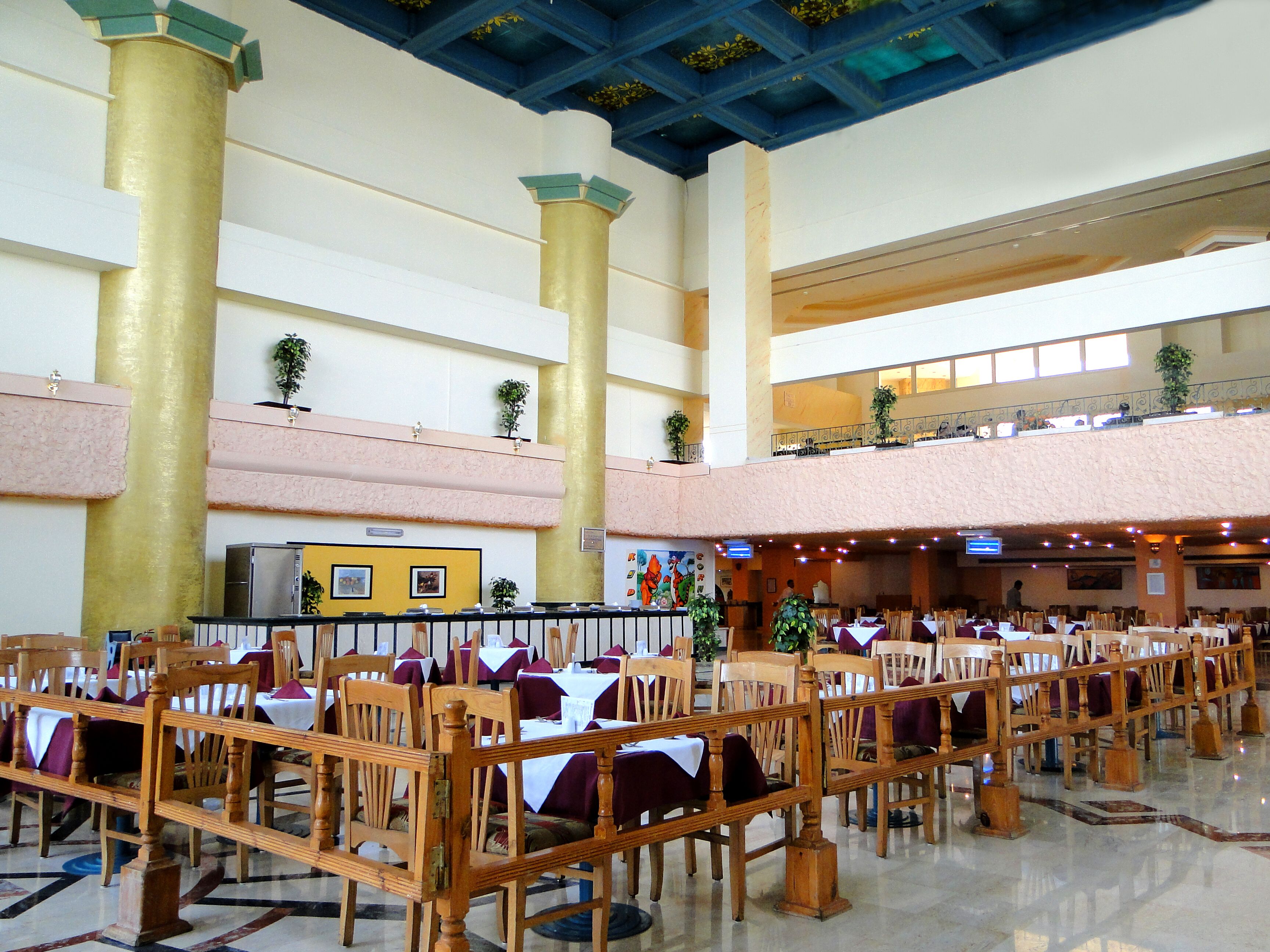 A spacious dining area with high ceilings, large golden columns, and multiple dining tables with chairs.