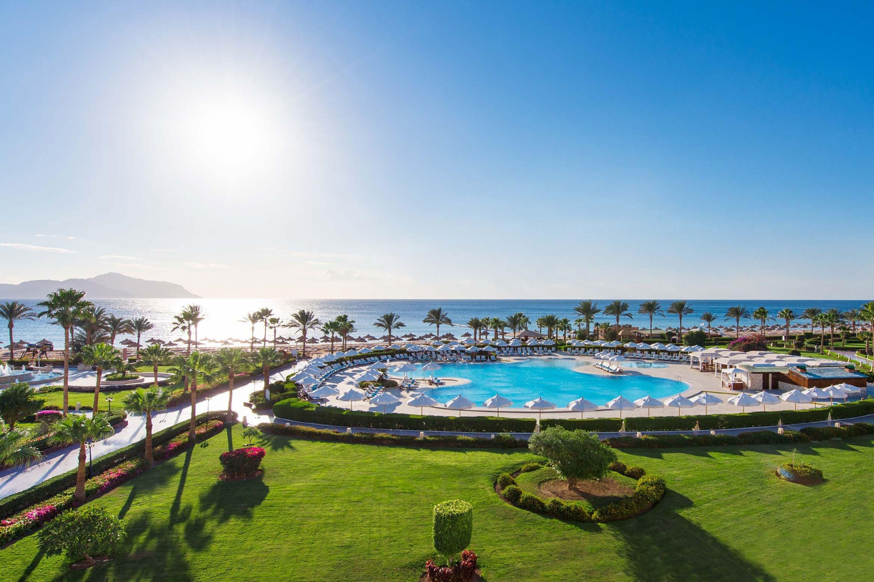 Ein Resort mit einem großen, runden Pool, Palmen und Blick auf den Ozean.