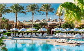 A pool area with lounge chairs and umbrellas, palm trees, and a view of the sea. - Baron Resort Sharm El Sheikh (Sharm El Sheikh)