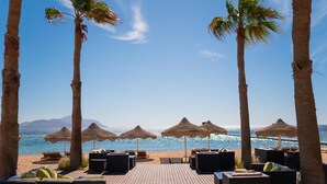 Un salon de plage doté de parasols en chaume, de chaises longues et d’une terrasse en bois offrant une vue sur la mer.