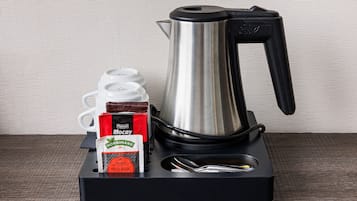 Una cafetera, un hervidor y una caja de cápsulas de café sobre una bandeja negra.