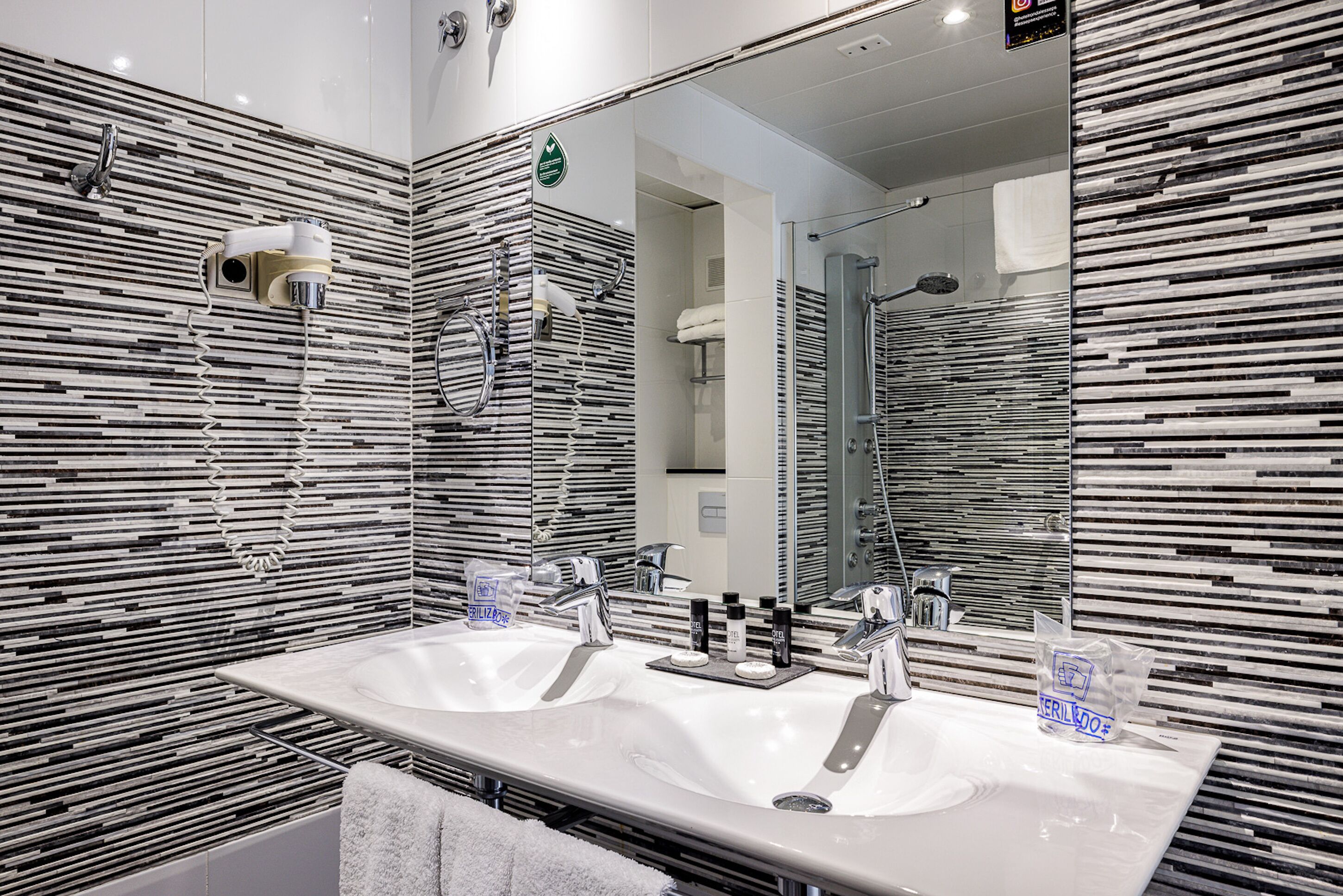 Un baño moderno con dos lavamanos, un espejo grande y una ducha.