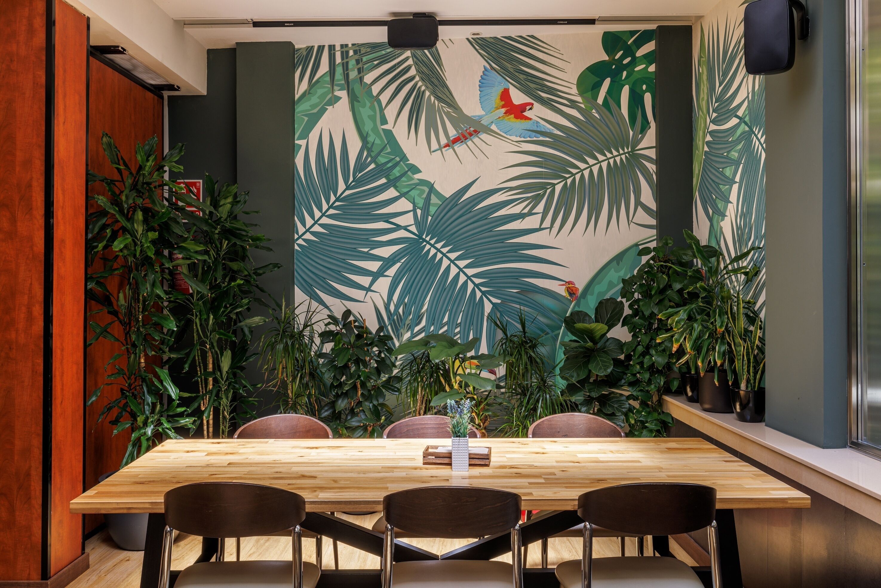 Un salón de conferencias con una mesa de madera, cuatro sillas y un gran mural con motivos tropicales en la pared.