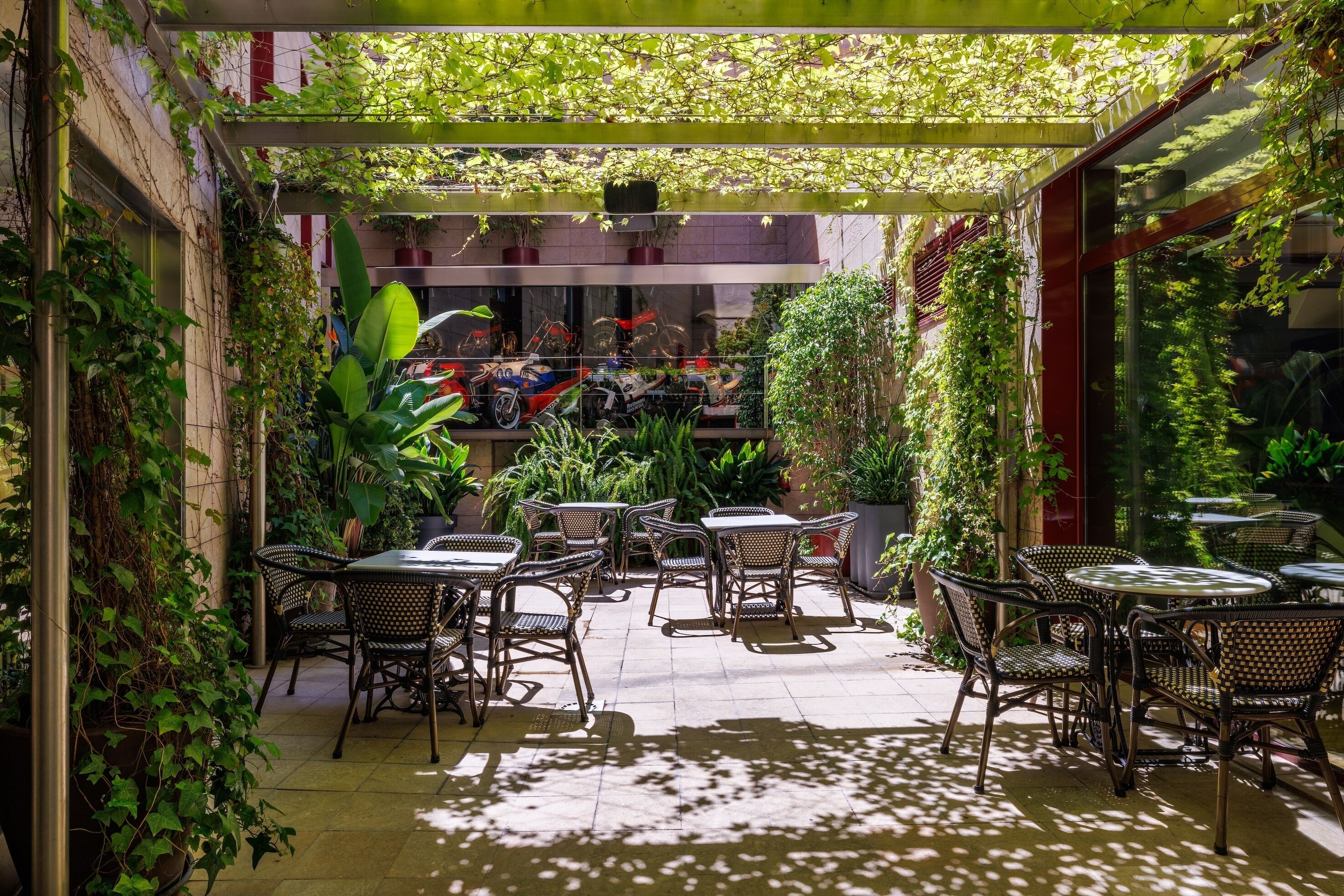 Een terras buiten met tafels en stoelen, omringd door weelderige begroeiing en potplanten.