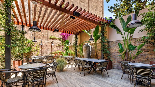 An outdoor patio with wooden tables and chairs, a brick wall, and potted plants.