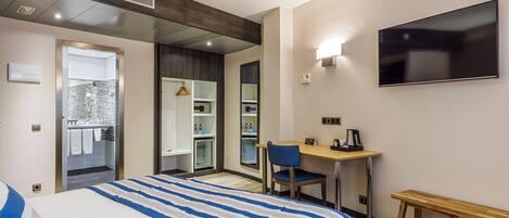 A hotel room with a bed, a desk, a chair, a TV, and a bench.
