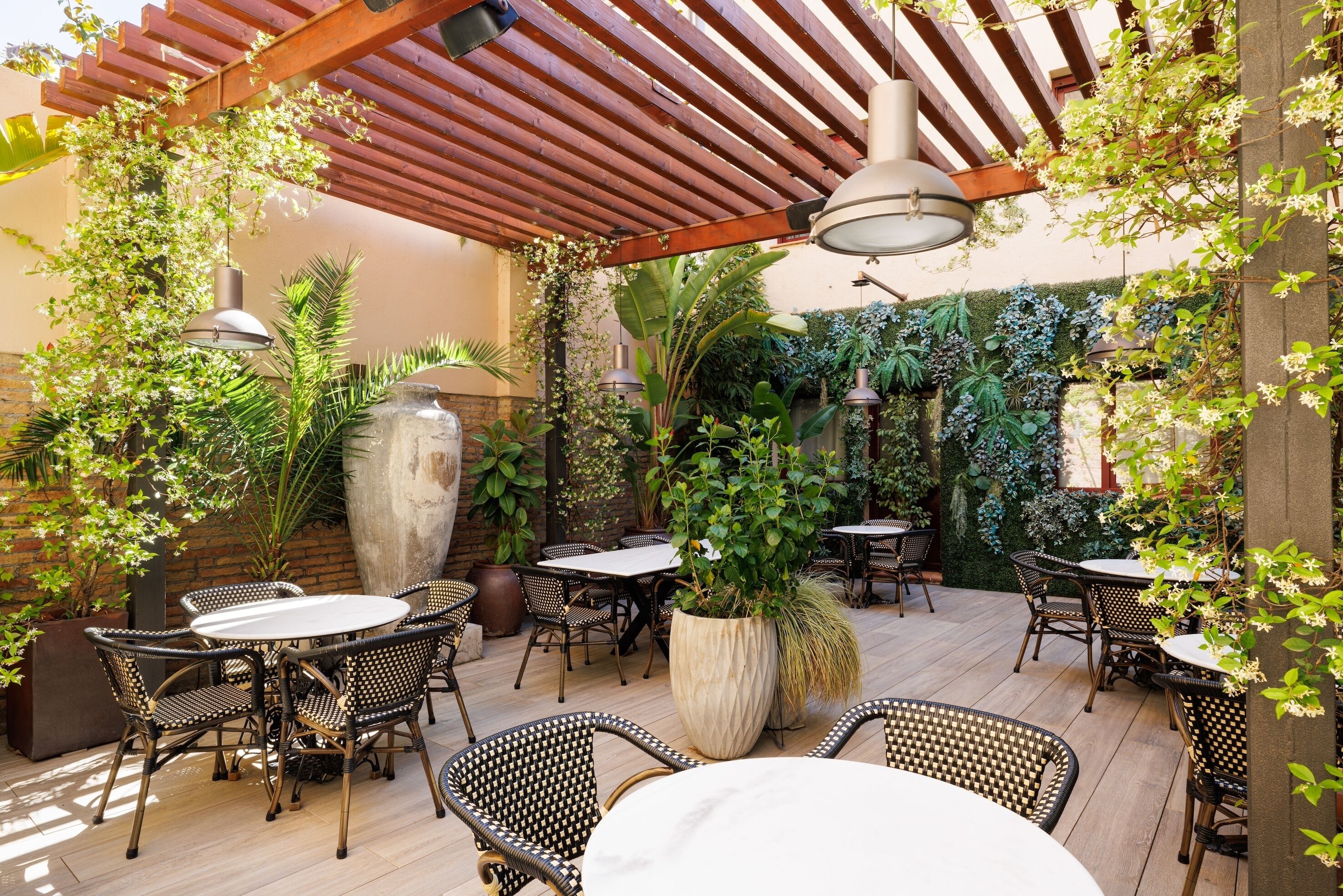 Une terrasse extérieure avec des tables rondes et des chaises en osier, entourée d’une végétation luxuriante et agrémentée d’une pergola en bois.