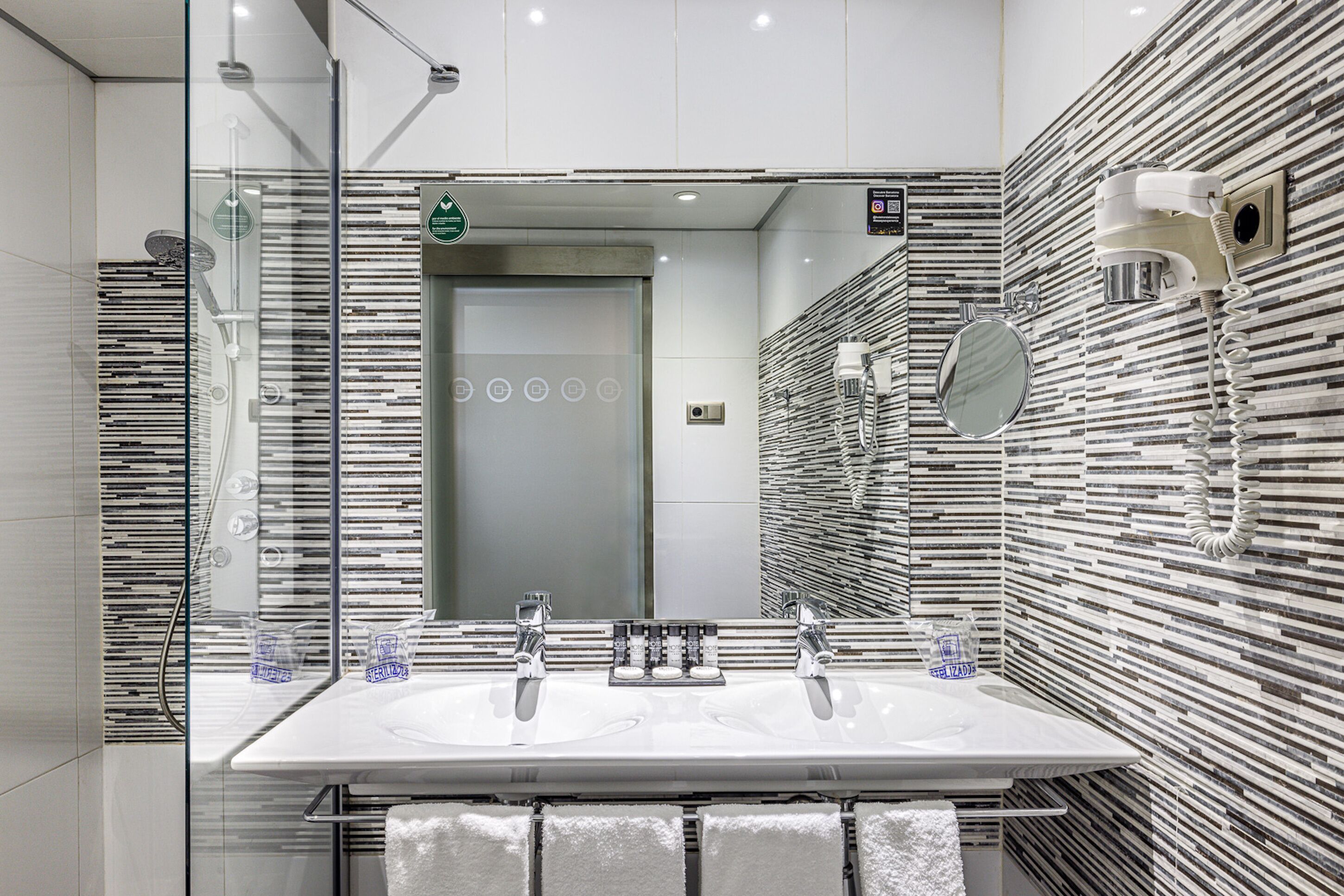 Un baño moderno con un espejo grande, dos lavamanos y una ducha con cerramiento de vidrio.