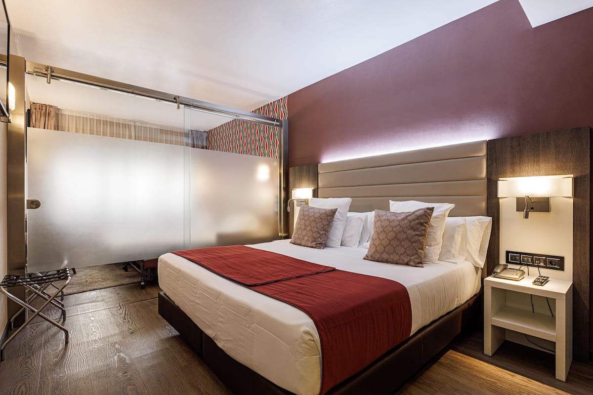 A hotel room with a large bed, a bedside table with a lamp, a wardrobe, and a mirror.