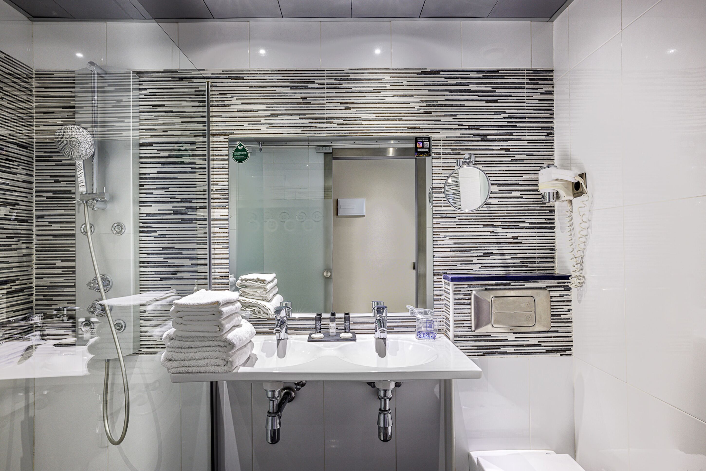 Un baño moderno con un espejo grande, un lavamanos, una ducha y un inodoro.