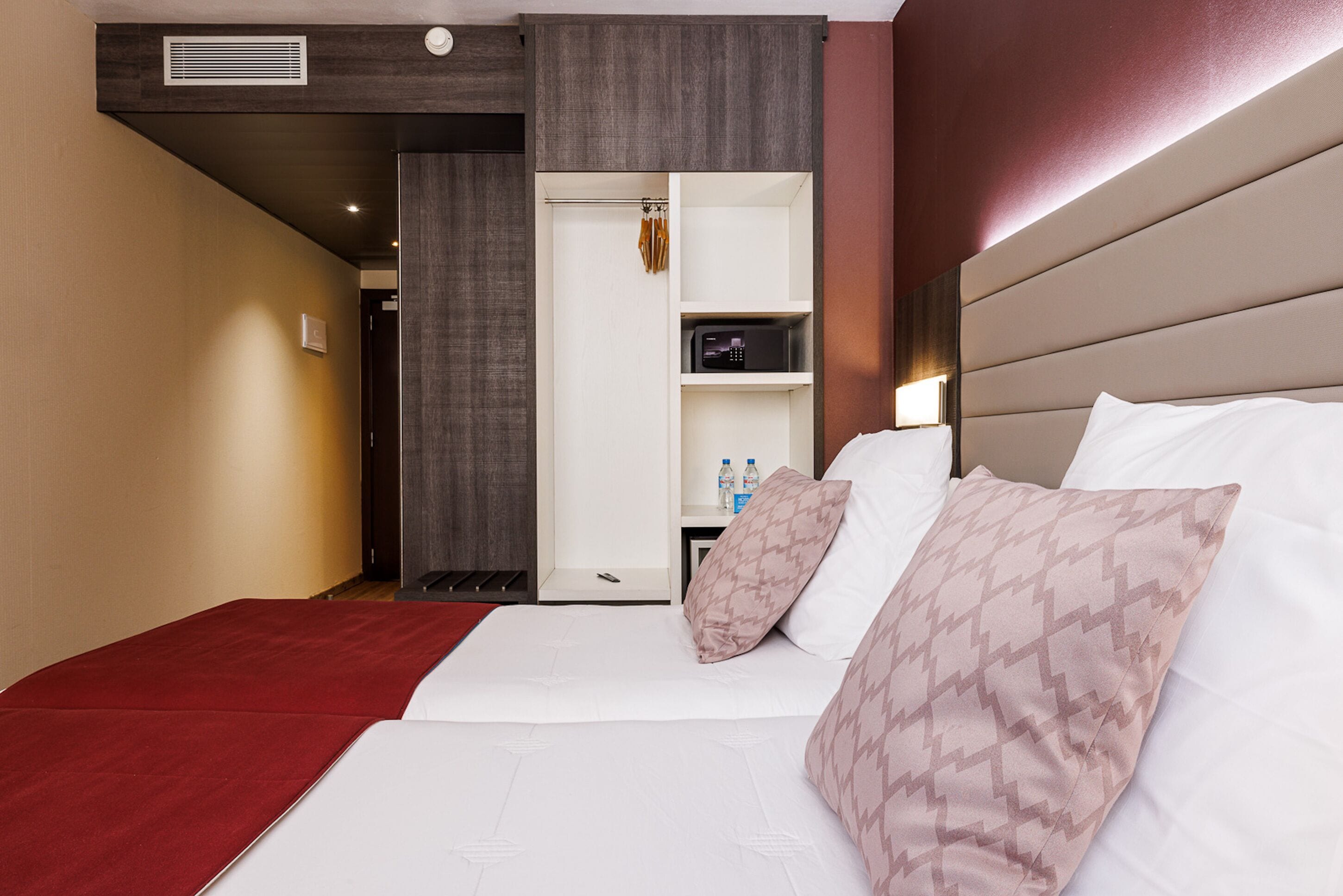 Hotellihuone, jossa on sänky, vaatekaappi ja pieni hylly, jossa on pulloja.