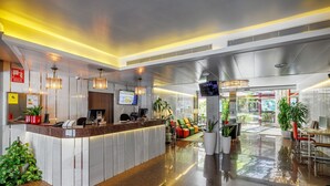 A modern hotel lobby with a reception desk, seating area, and large windows.