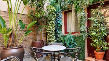 Un patio con sillas de mimbre, una mesa redonda y plantas en macetas.