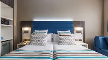 Una cama doble con ropa de cama a rayas, dos mesitas de noche con lámparas, un cabecero azul y un minibar.