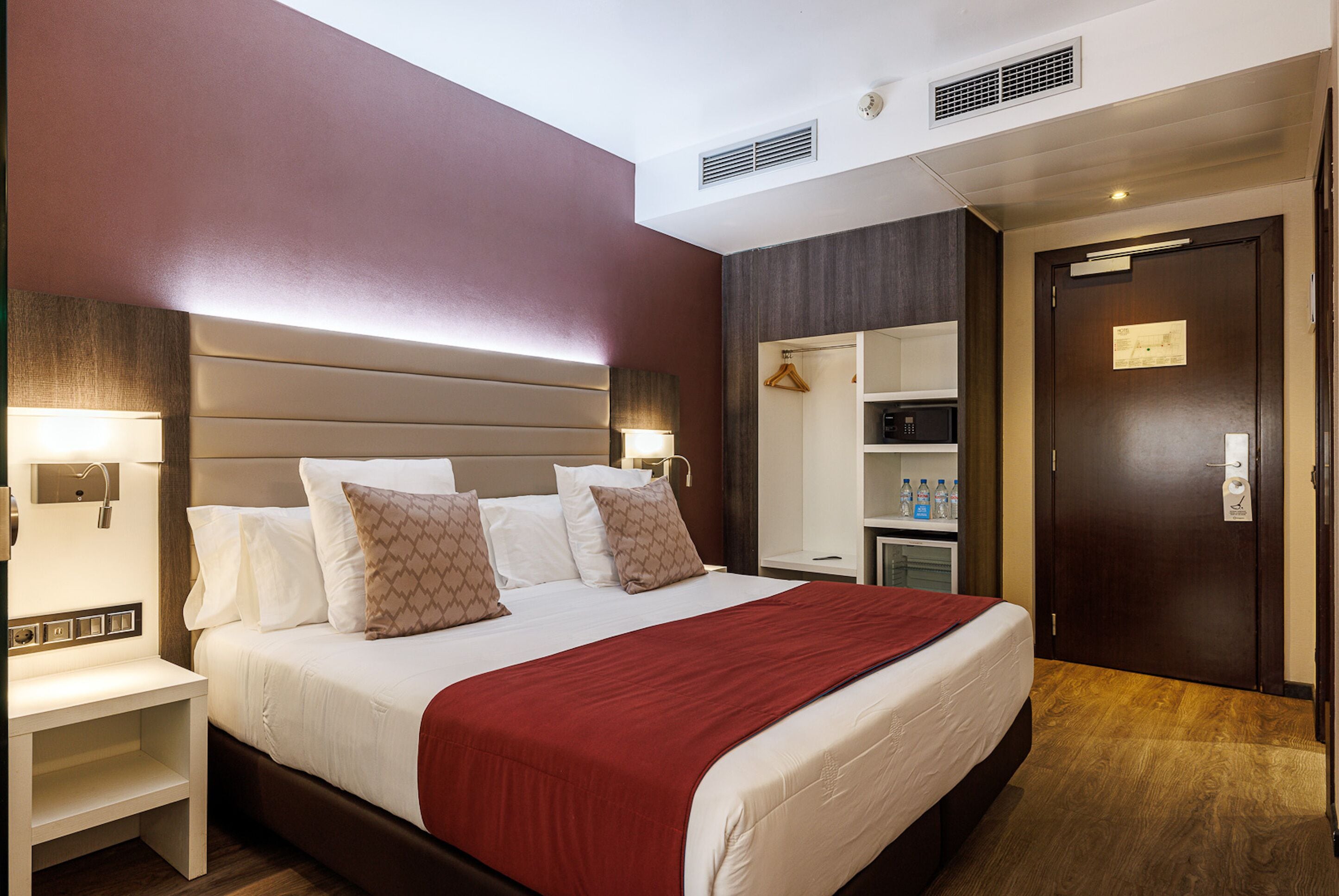 A hotel room with a large bed, bedside tables, a wardrobe, and a mirror.