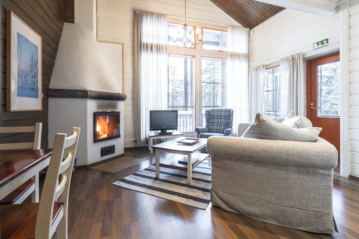 A cozy living room with a fireplace, wooden furniture, and large windows.