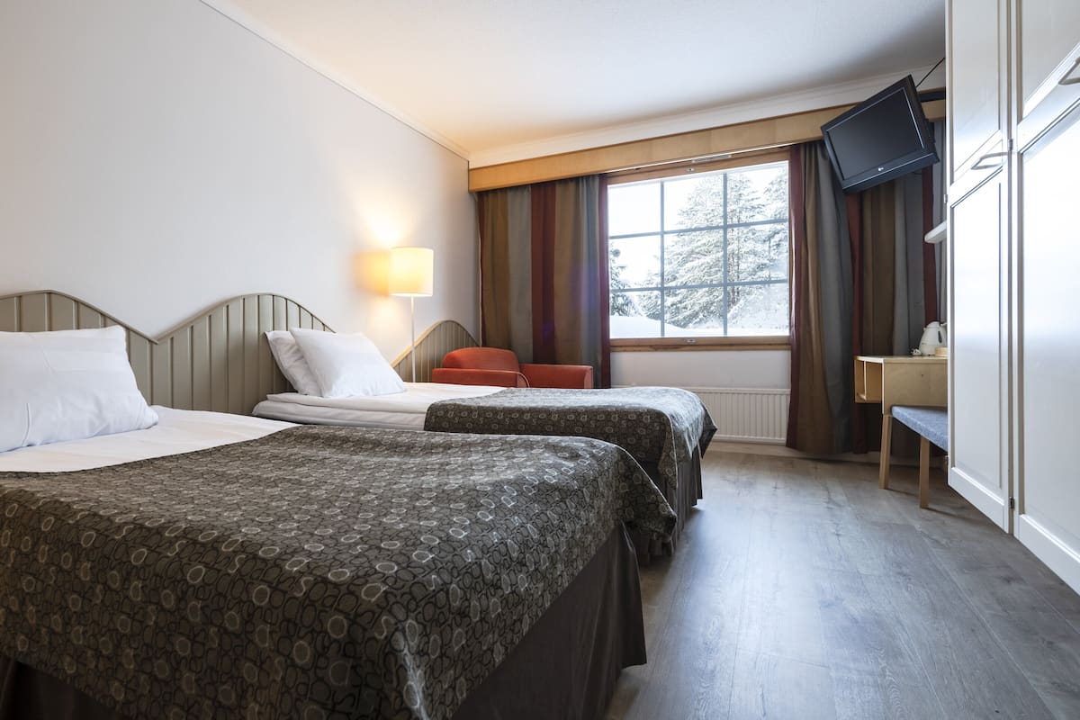 A hotel room with two beds, a desk, a television, and a window with curtains.