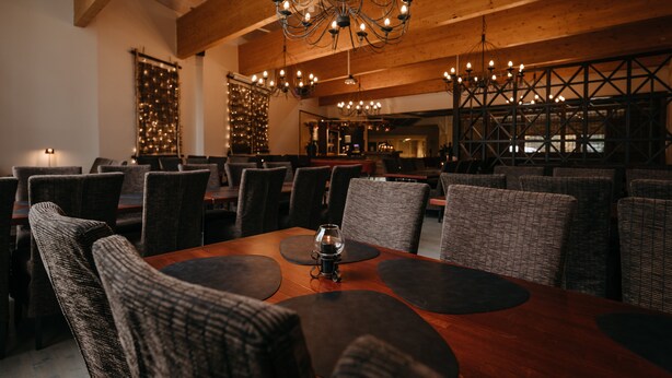 Un restaurante con vigas de madera, mesas redondas con posavasos negros y una araña.