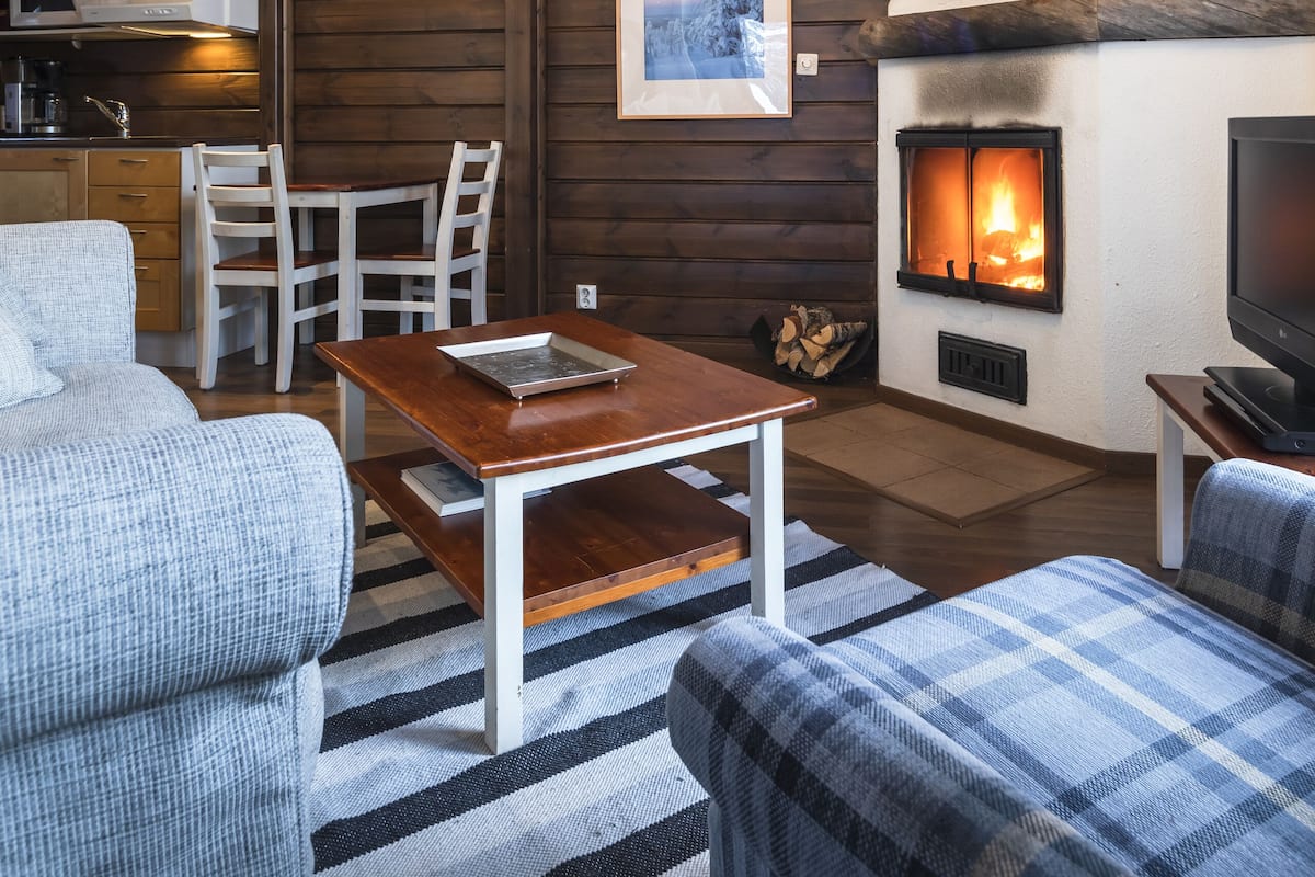 A cozy living room with a fireplace, wooden ceiling, and a dining area with chairs and a table.