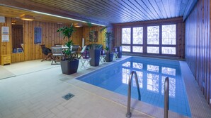 Una piscina interior con paredes y techo de madera, rodeada de asientos y plantas en macetas.