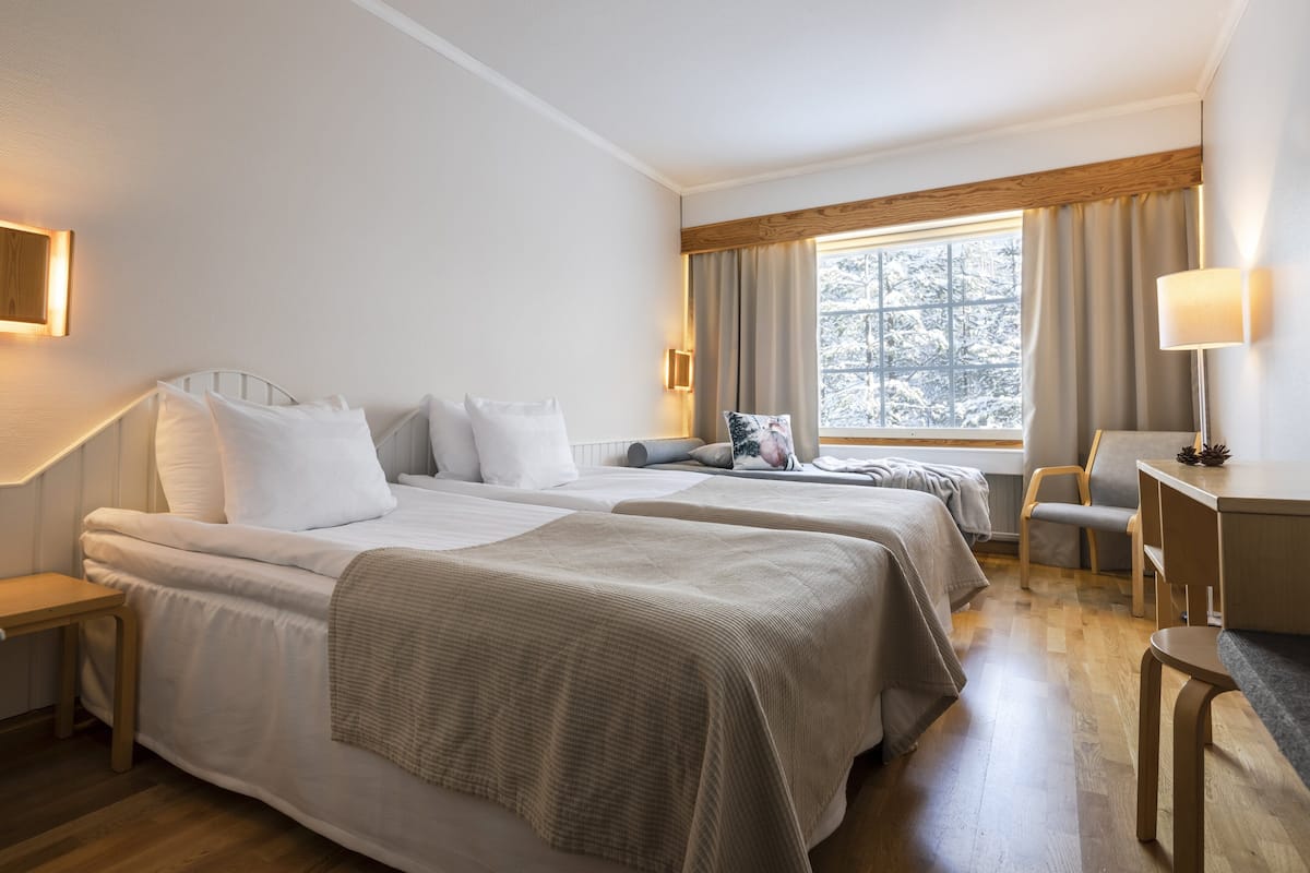 A hotel room with two beds, a desk, a chair, and a window with curtains.
