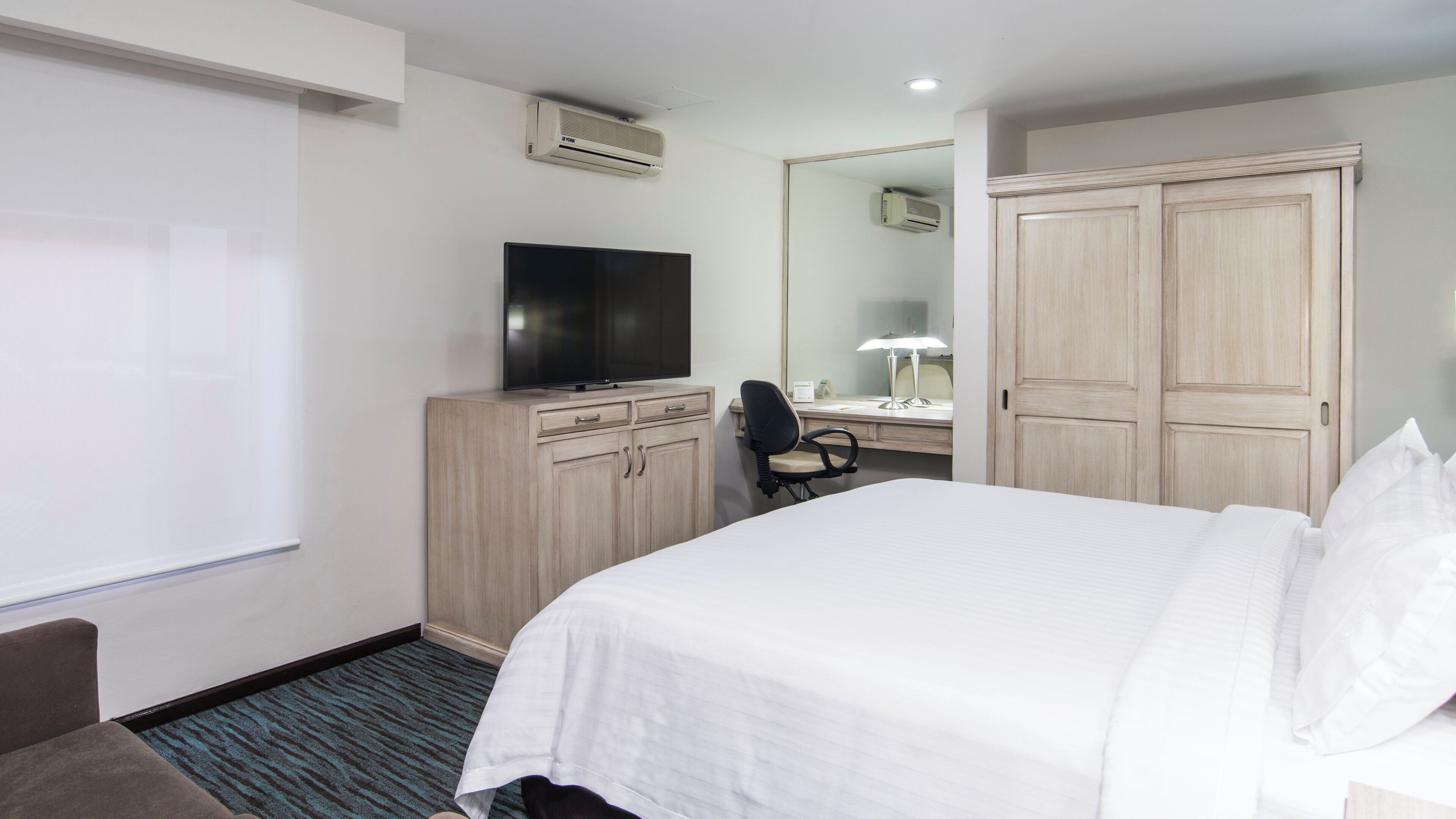 Una habitación de hotel con cama, escritorio con silla, televisión y armario.